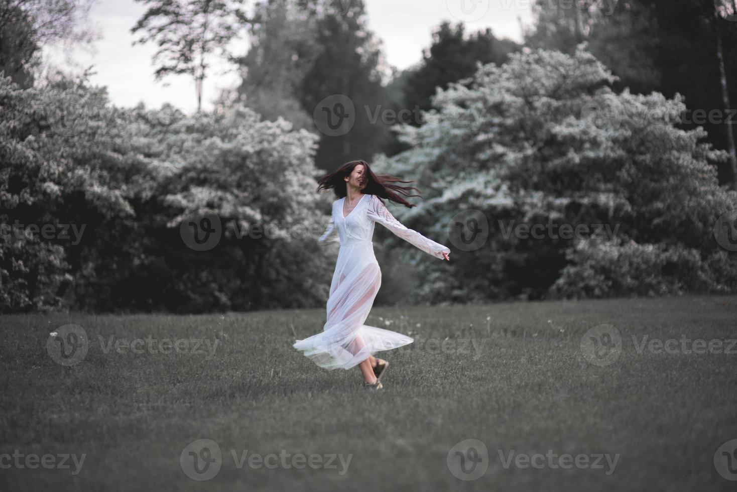 donna felice in abito bianco che balla in un parco cittadino in fiore foto