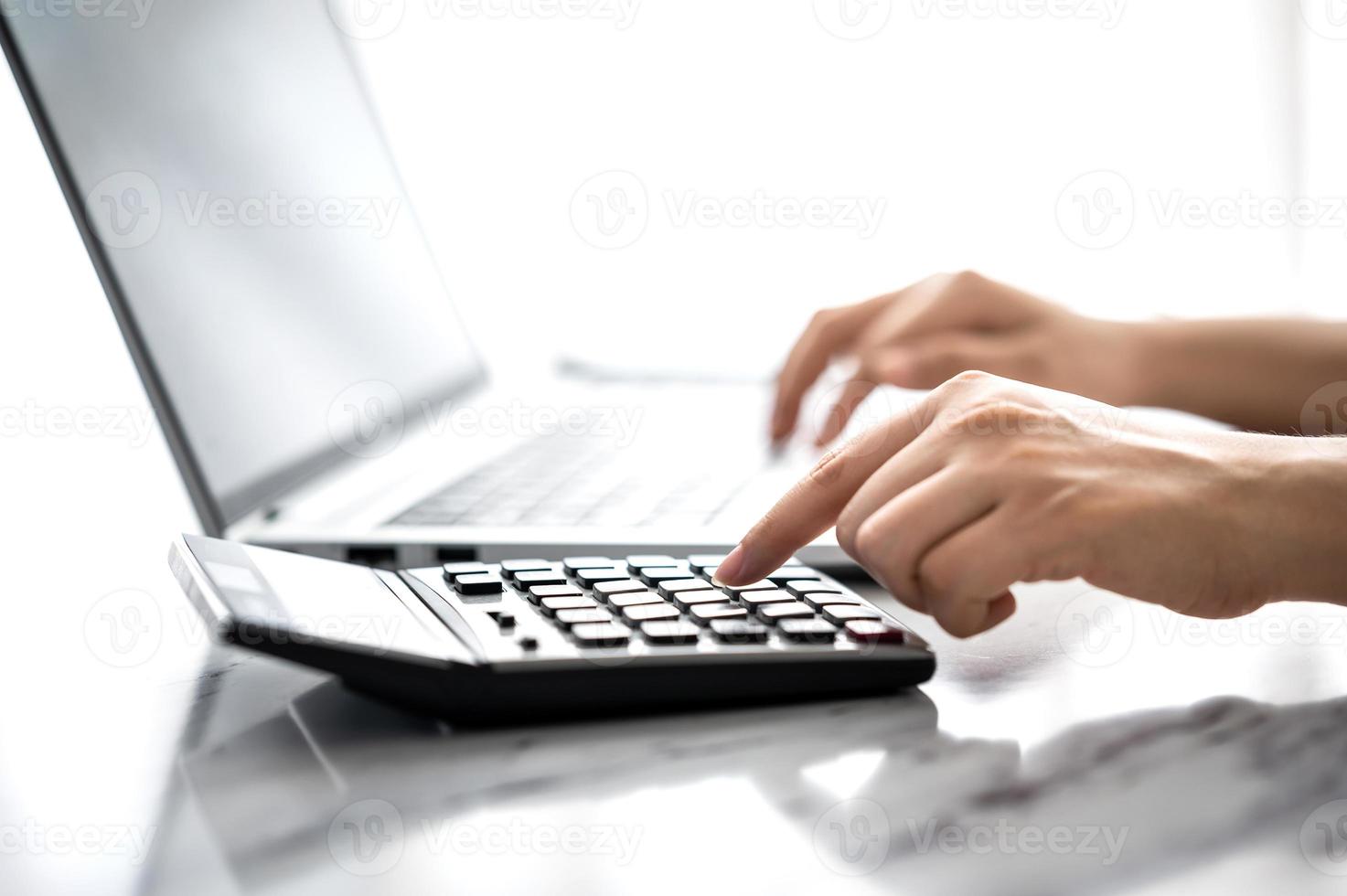 mano di donna che usa calcolatrice e laptop foto