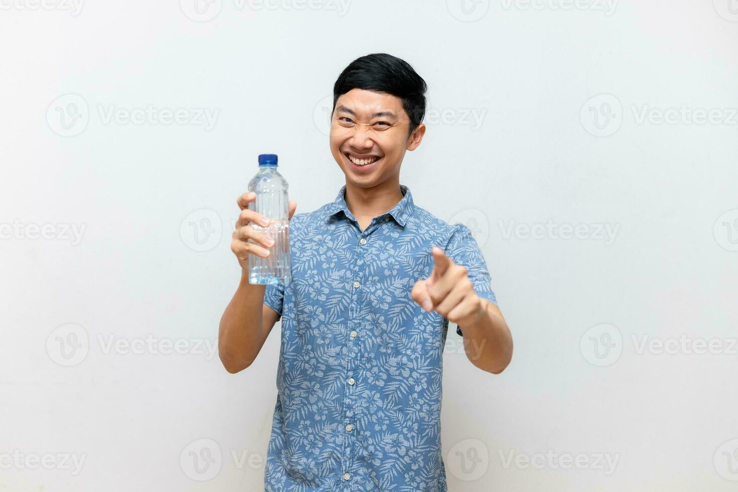 positivo asiatico uomo blu camicia Tenere acqua bottiglia con punto dito a voi contento Sorridi isolato foto