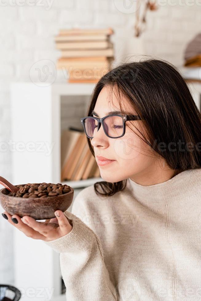 donna che prepara il caffè nella caffettiera, annusando i chicchi di caffè foto