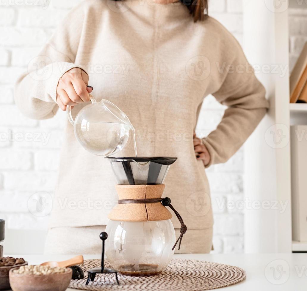 donna che prepara il caffè nella caffettiera, versando acqua calda nel filtro foto