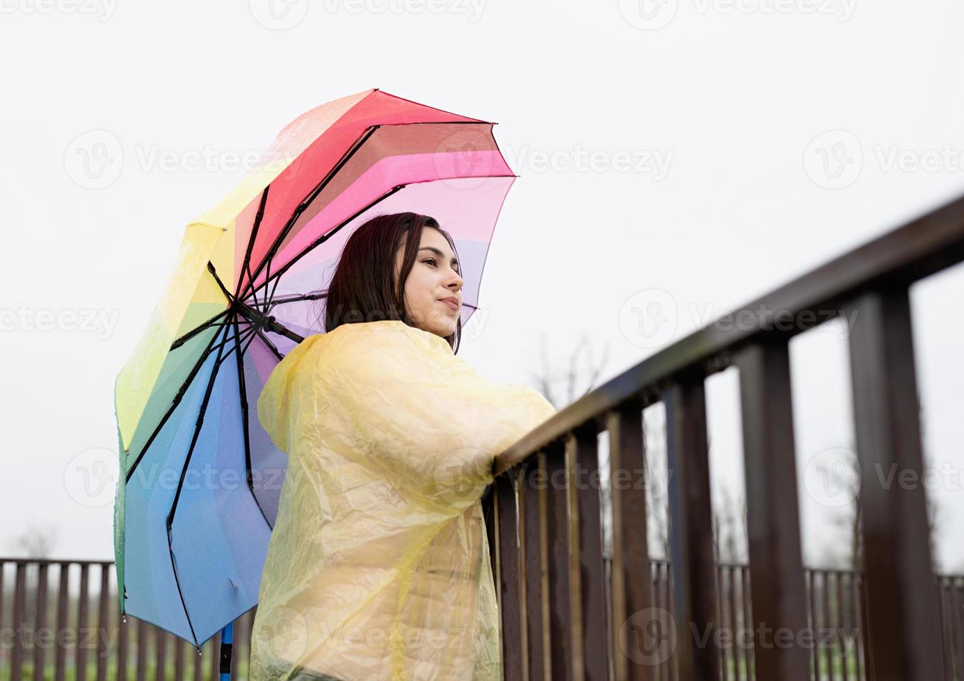 donna in piedi all'aperto con in mano un ombrello colorato, distogliendo lo sguardo foto