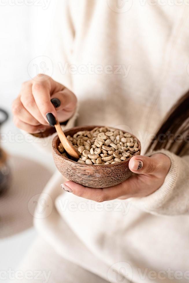 mano di donna che tiene ciotola con chicchi di caffè verde foto