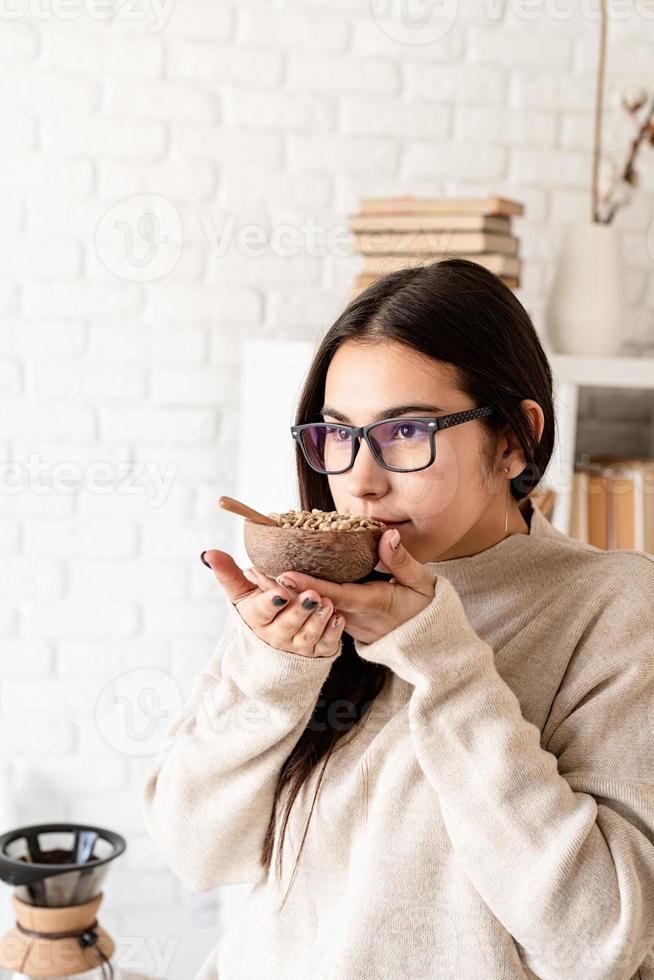 donna che prepara il caffè nella caffettiera, annusando i chicchi di caffè verde foto