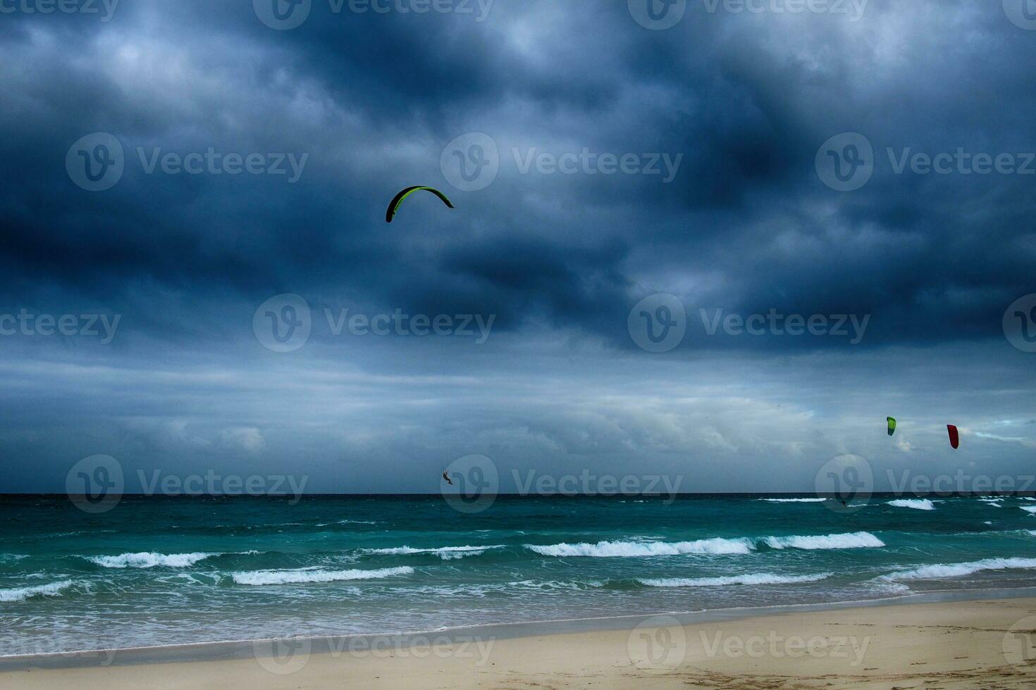 estate paesaggio con il oceano con buio nuvoloso onde e surfermi kit con paracadute galleggiante su il riva foto
