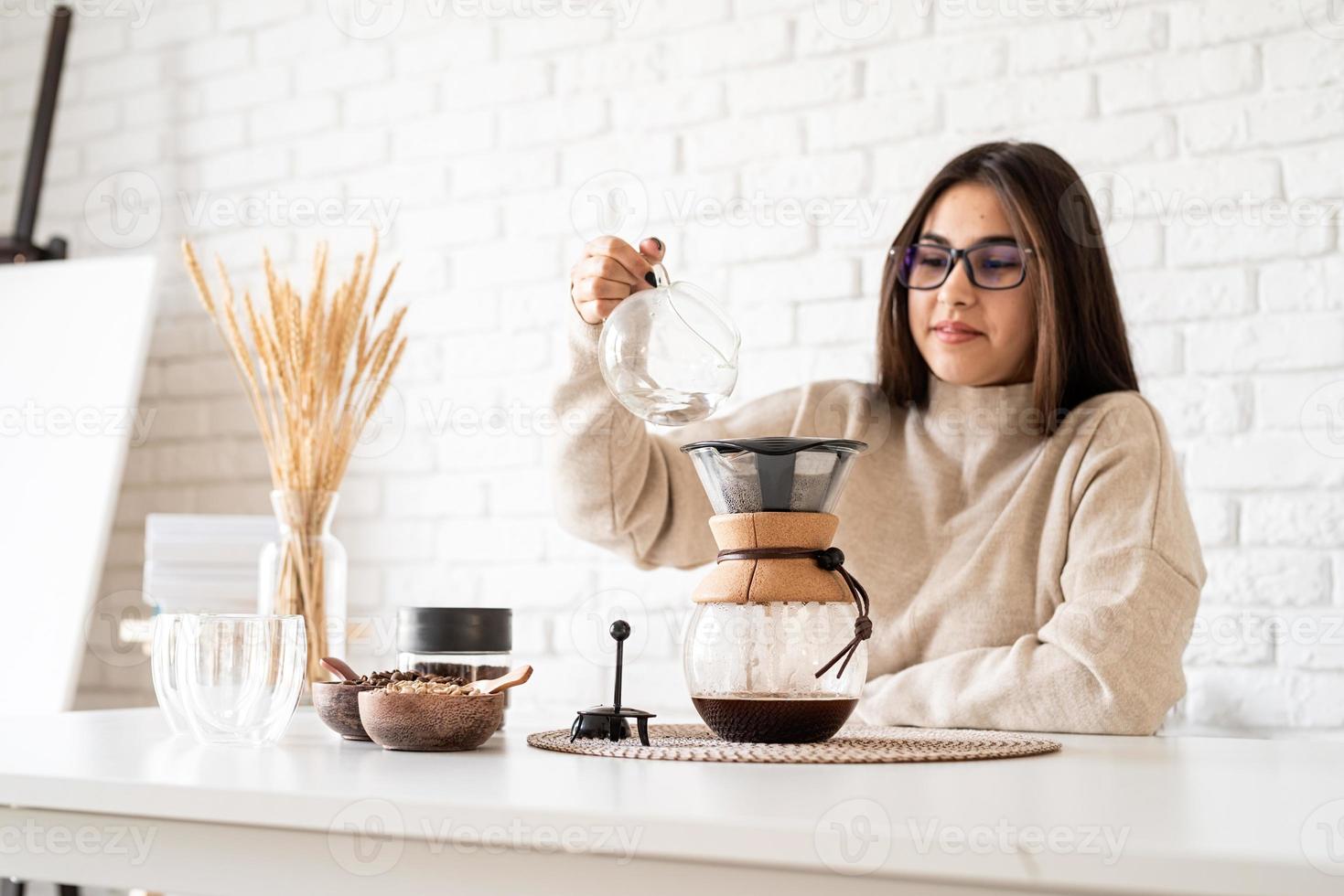 donna che prepara il caffè nella caffettiera, versando acqua calda nel filtro foto