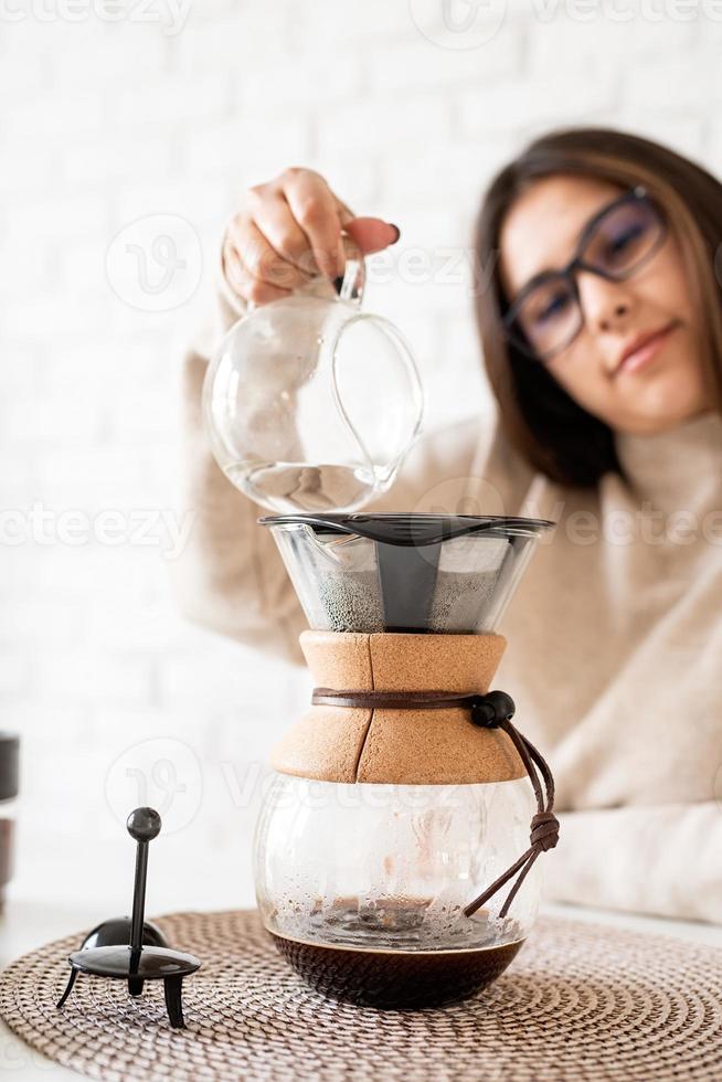 donna che prepara il caffè nella caffettiera, versando acqua calda nel filtro foto