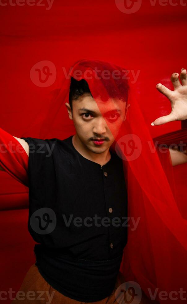 un asiatico uomo in piedi nel davanti di un' rosso stoffa con un' rosso stoffa sospeso al di sopra di il suo testa foto