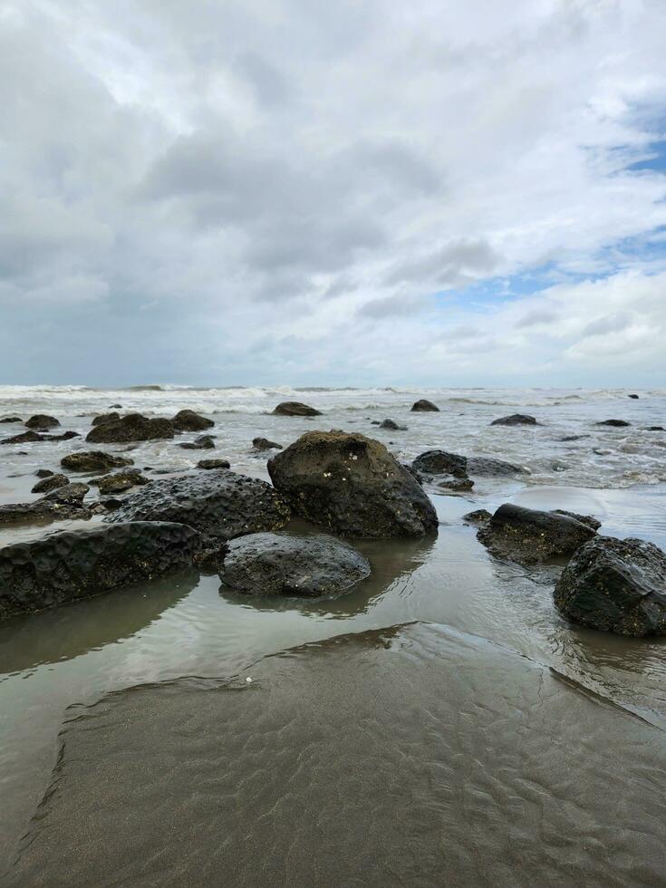 mare su un' nuvoloso giorno bianca sabbioso spiaggia con pietra foto