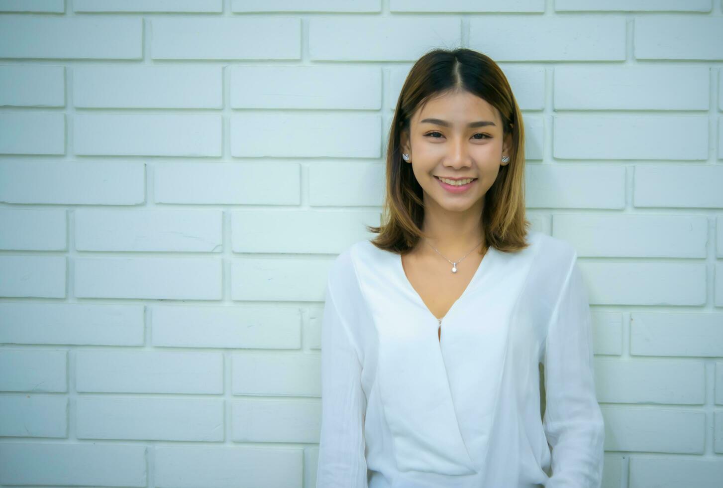bellissimo asiatico donna d'affari è in piedi dritto e sorridente mentre guardare a il telecamera su un' bianca mattone sfondo, digitale marketing. foto