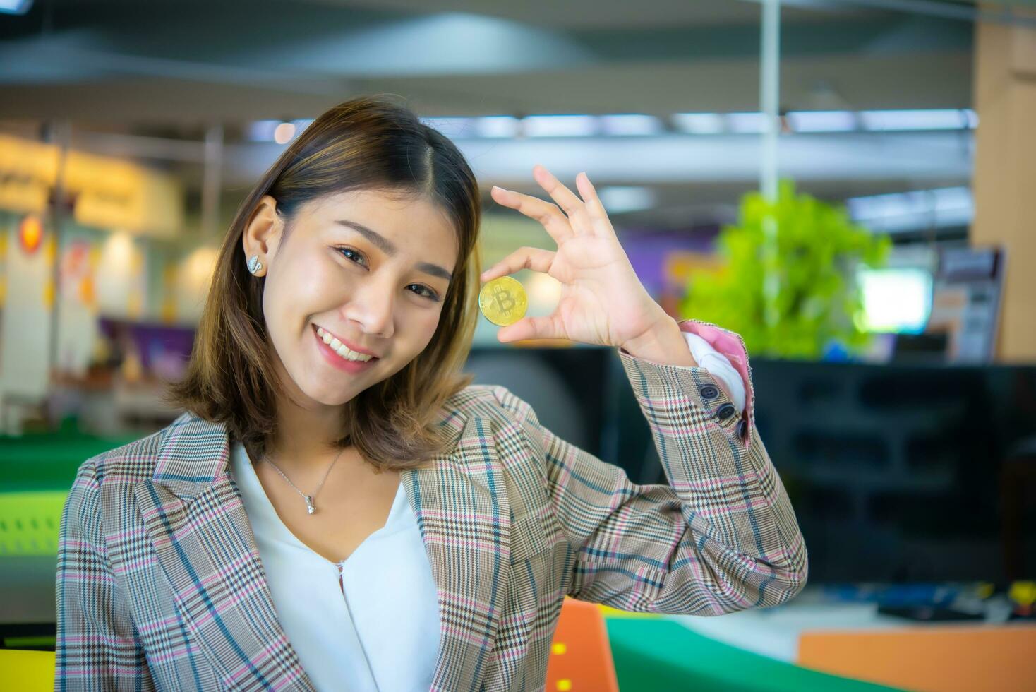 bellissimo asiatico attività commerciale donna Tenere virtuale moneta bitcoin fare ok cartello con dita, sorridente amichevole Esprimere a gesti eccellente simbolo. foto