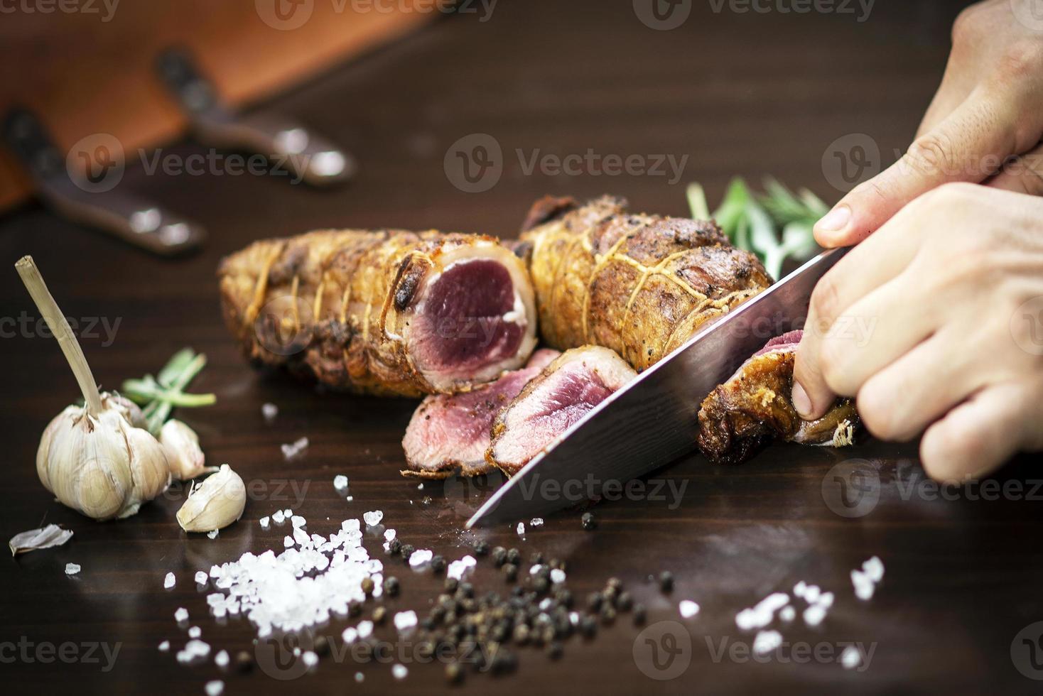 Affettare una porzione di organic roast beef roll con coltello sul tavolo di legno con aglio pepe e sale a Melbourne in Australia foto