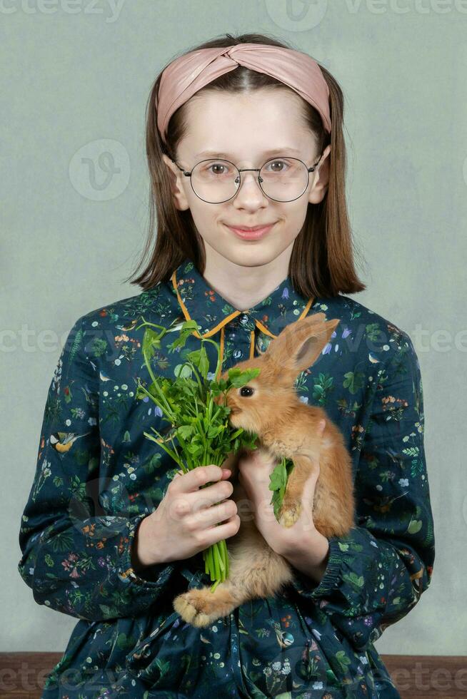 divertente ragazza nel bicchieri feed un' rosso coniglio con prezzemolo. foto