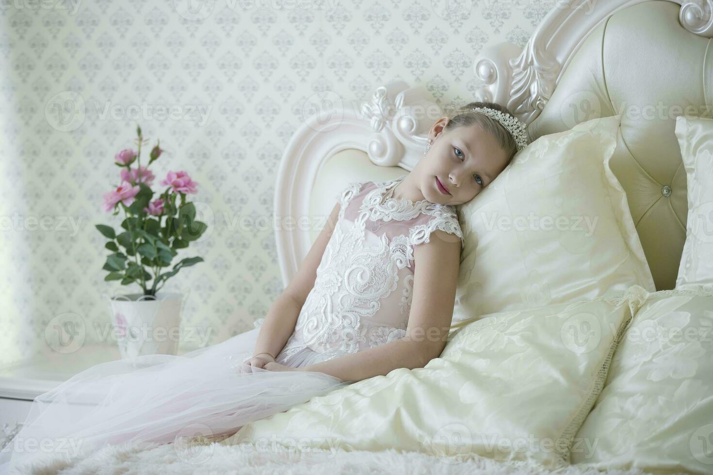 carino tenero ragazza adolescente bugie su il letto. Principessa nel un' bianca vestito con un' corona. foto