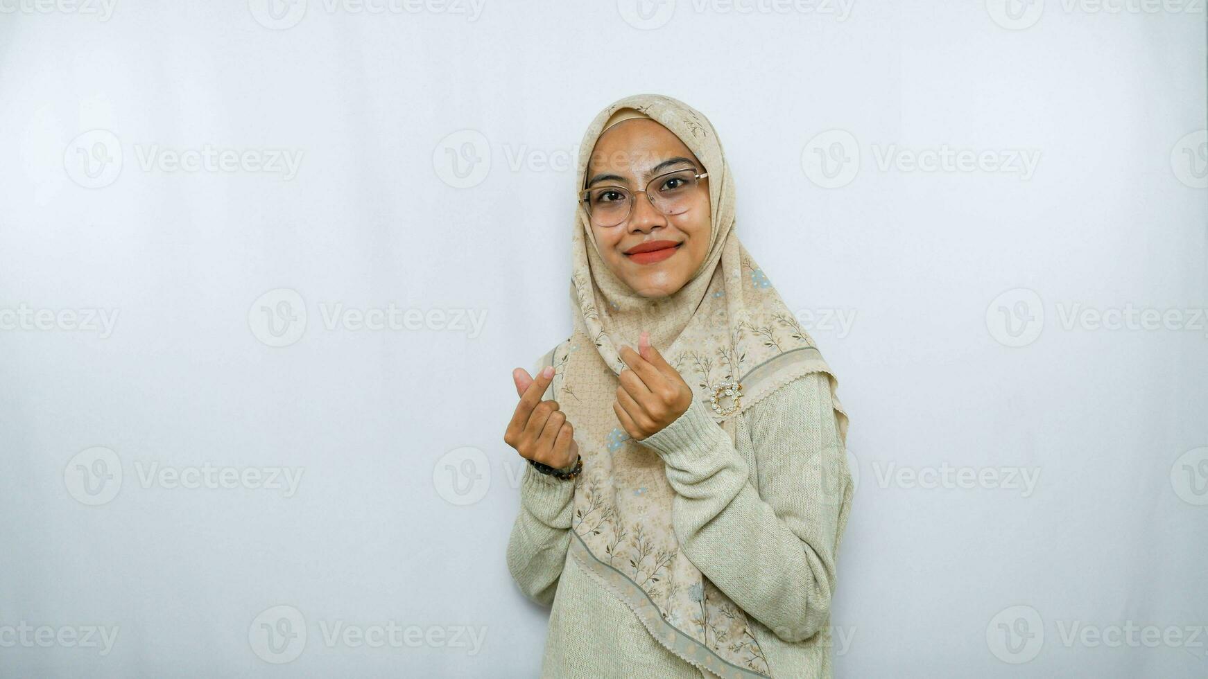 bellissimo sorridente asiatico donna nel tradizionale musulmano vestito mostrando coreano cuore con Due dita attraversato, esprimere gioia e positività isolato al di sopra di bianca sfondo foto