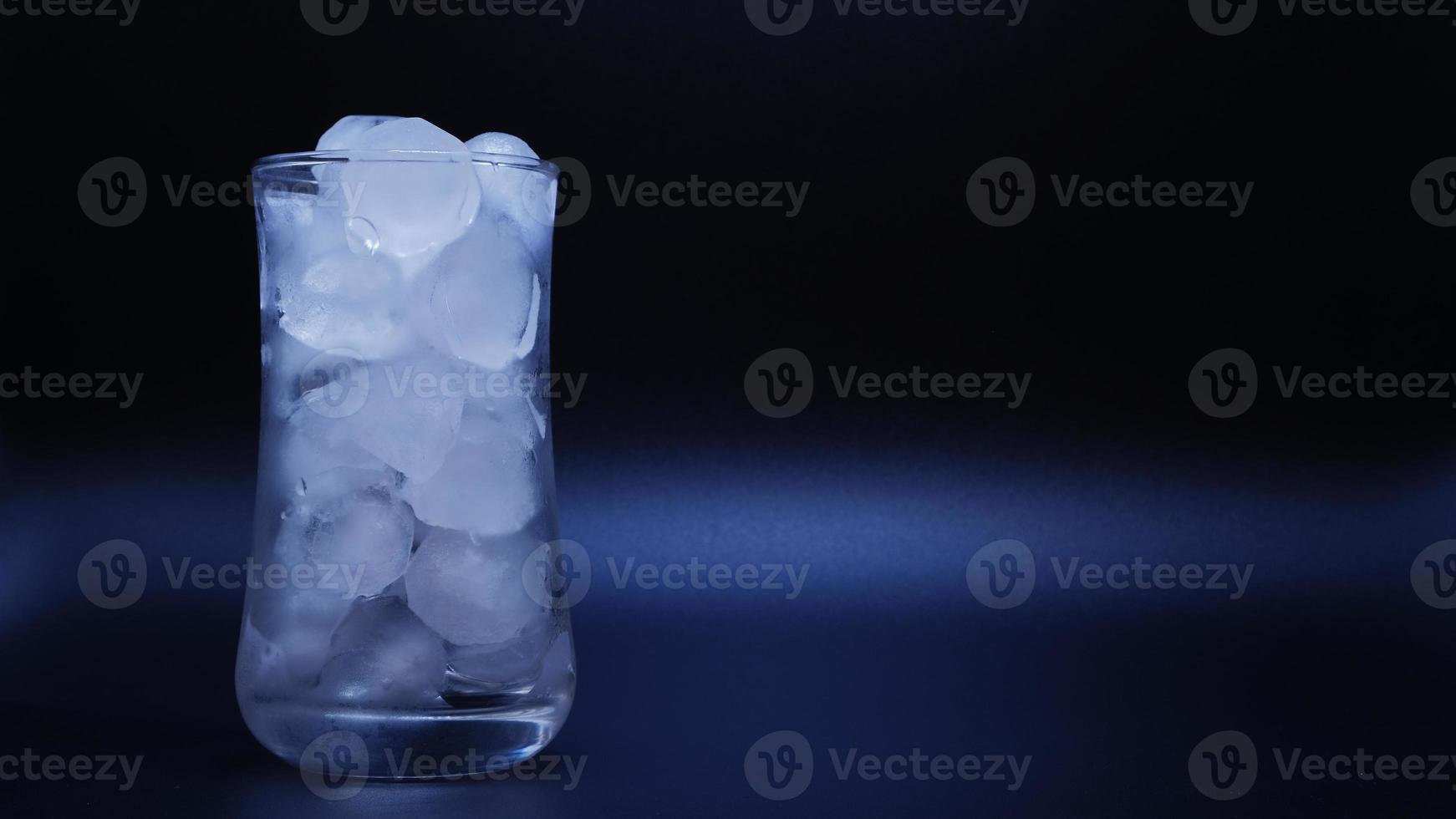 il ghiaccio in un bicchiere d'acqua che si scioglie su sfondo nero. foto