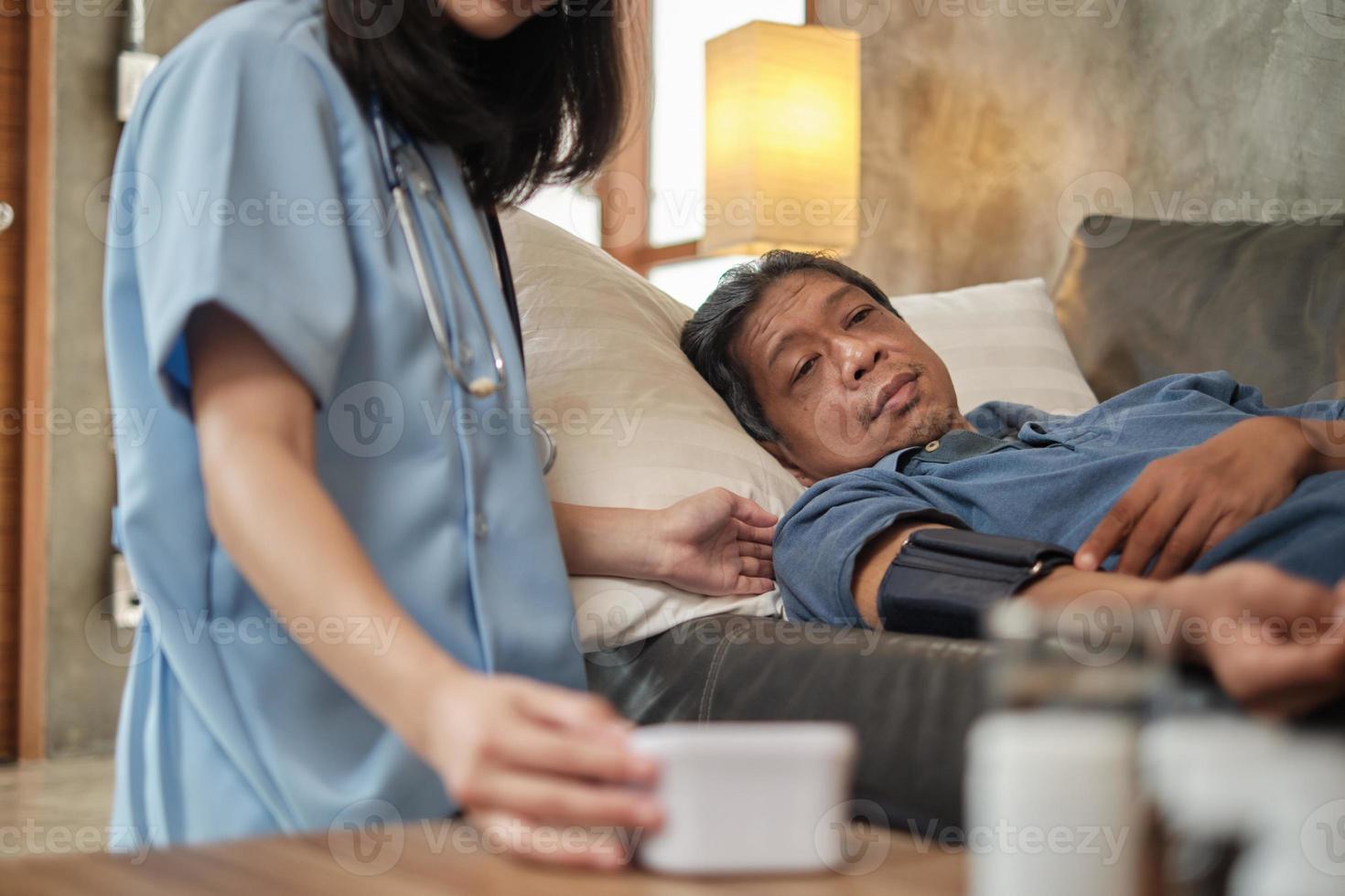 medico femminile che controlla la salute del paziente maschio anziano asiatico a casa. foto