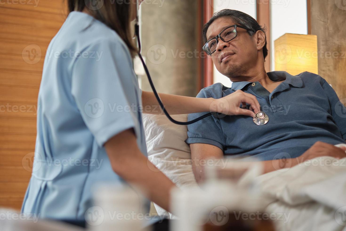 medico femminile che controlla la salute del paziente maschio anziano asiatico a casa. foto