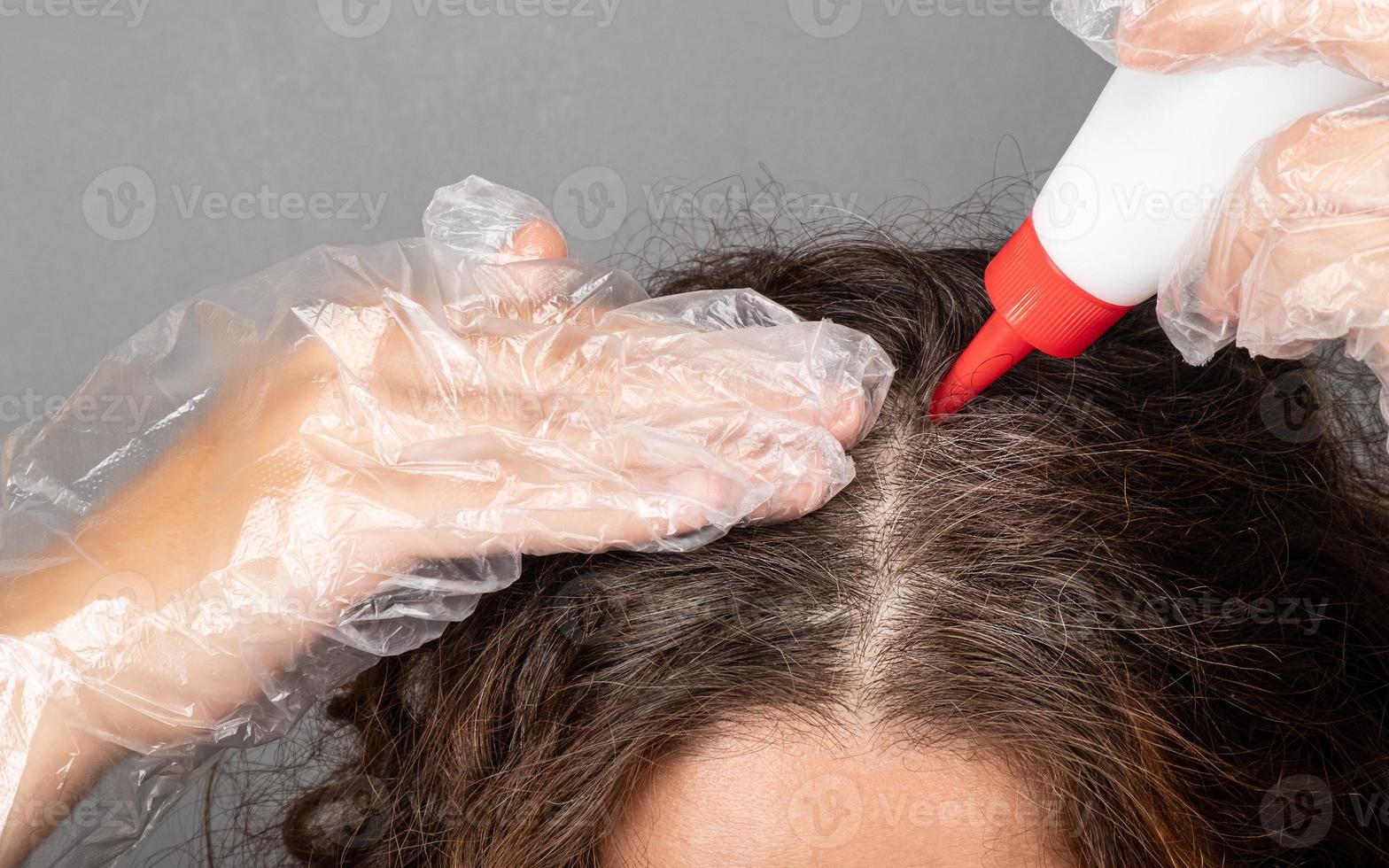 una donna applica la tintura alle radici dei suoi capelli dipinge i capelli grigi grigi. foto