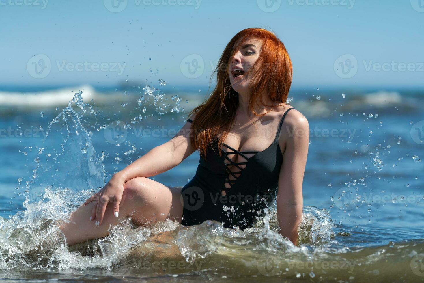 testa Rossa donna nel costume da bagno nel spruzzi acqua rottura mare onde, facciale espressione di giocoso femmina foto