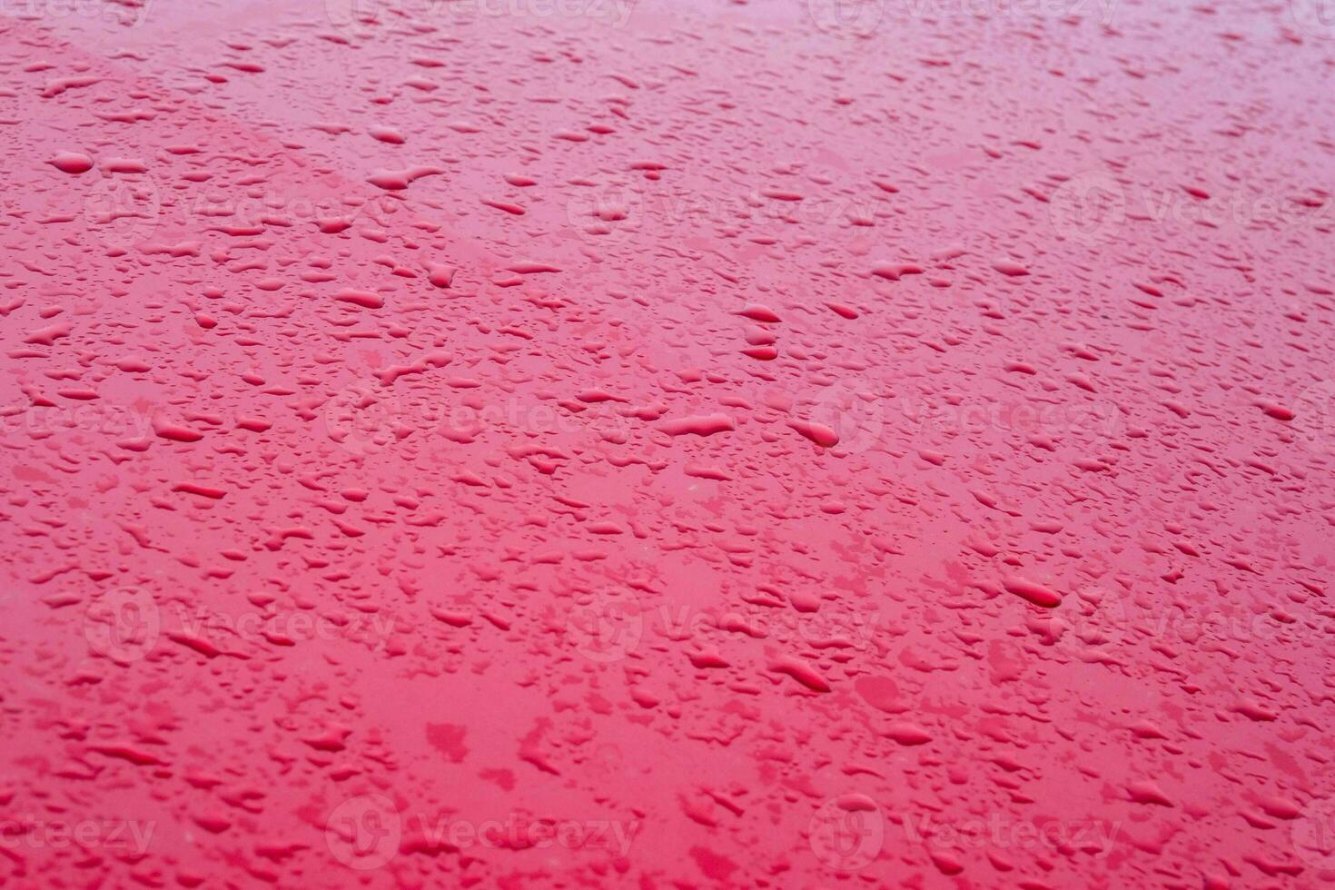 acqua goccioline a partire dal pioggia su un' rosso metallo cappuccio di un' macchina. pioggia gocce su rosso auto cappuccio. selettivo messa a fuoco foto