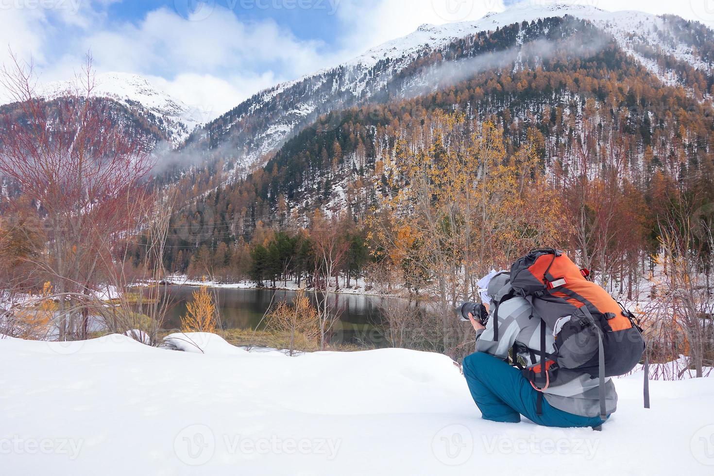 fotografo sulla neve in autunno davanti a un lago di montagna foto