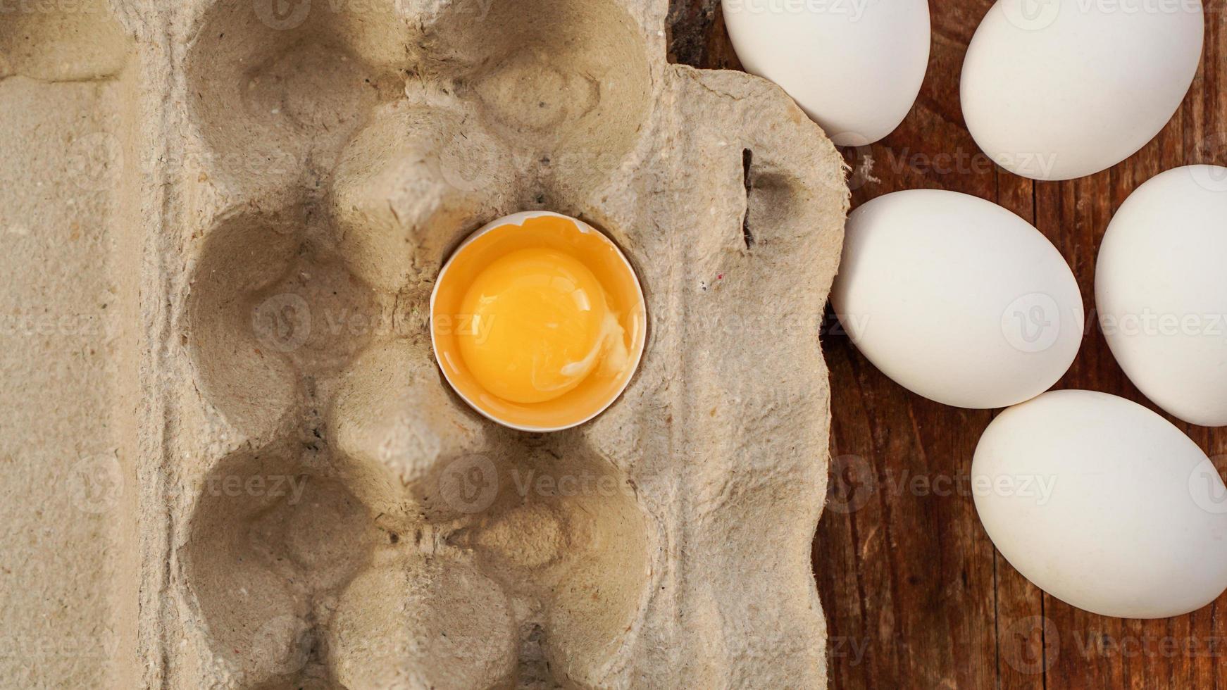 cartone di uova bianche e metà dell'uovo incrinato con vista dall'alto del tuorlo foto