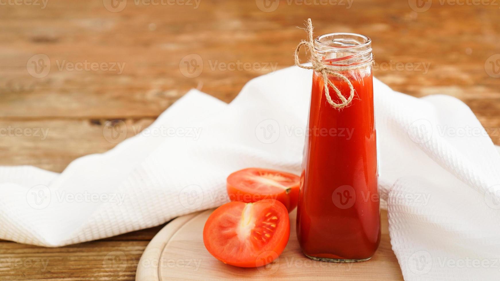 succo di pomodoro in bottiglia di vetro e pomodori freschi su fondo in legno foto