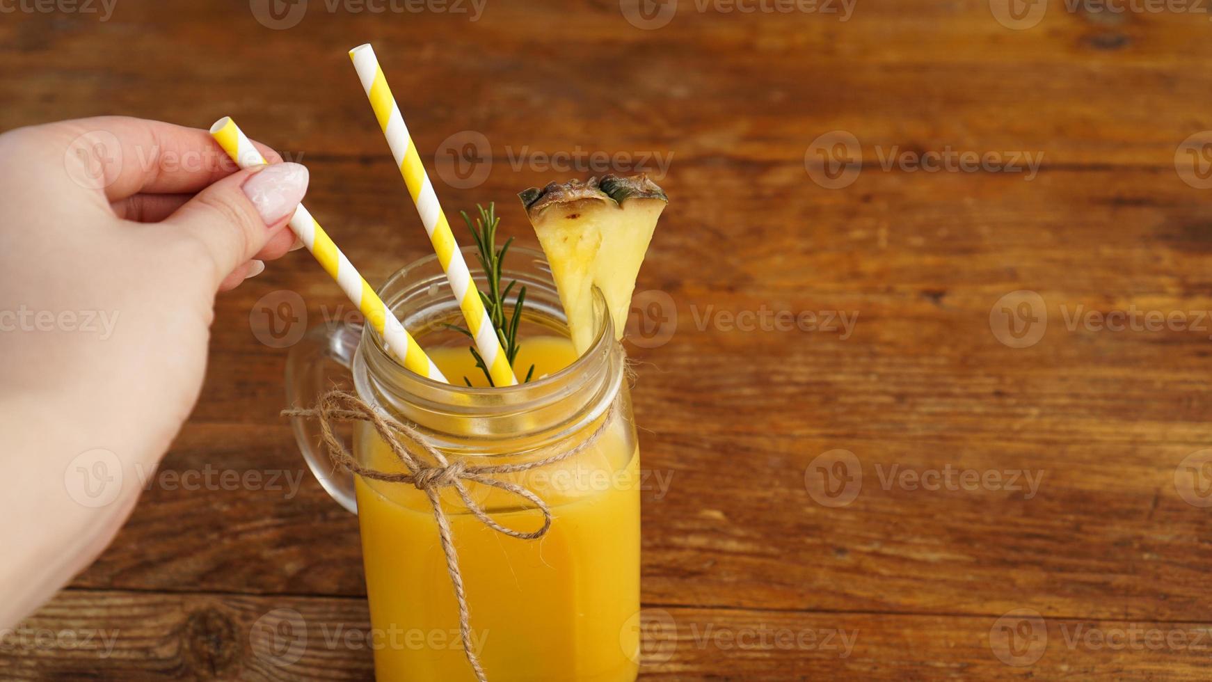 la mano della donna tiene una cannuccia, un bicchiere di succo d'ananas fresco foto