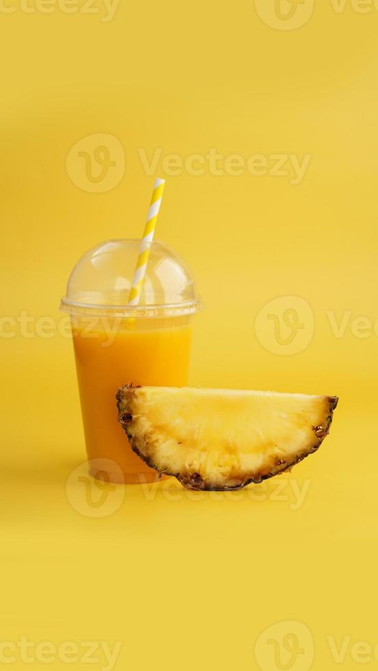 succo d'ananas in un bicchiere di plastica su sfondo giallo foto