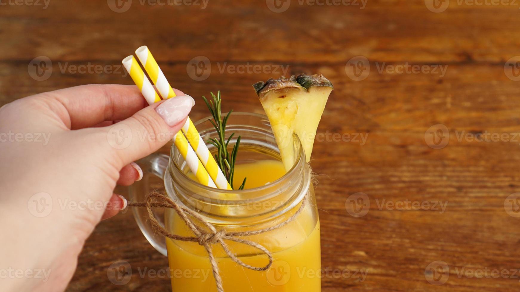 la mano della donna tiene una cannuccia, un bicchiere di succo di ananas fresco, primo piano foto