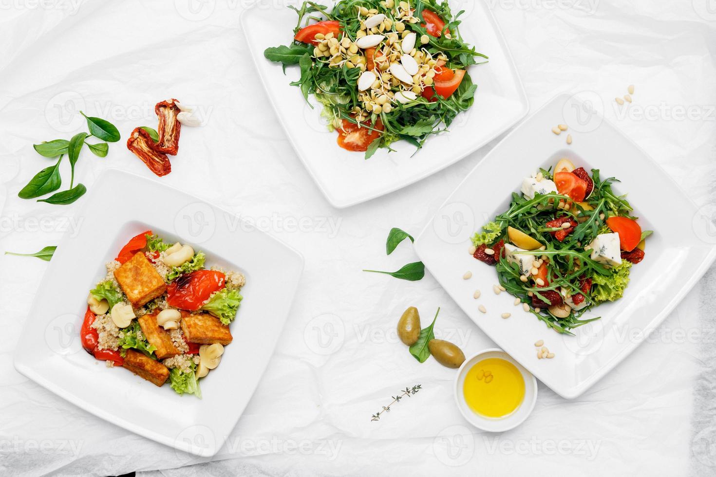 tre piatti bianchi con insalata, rucola, olive su fondo bianco foto