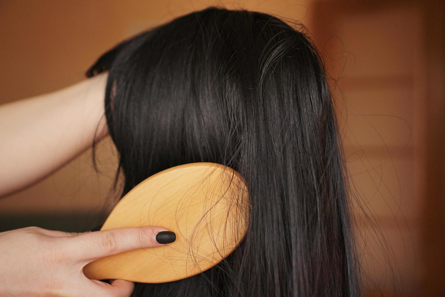 la mano femminile tiene una parrucca nera con i capelli lunghi e pettina un pettine di legno foto