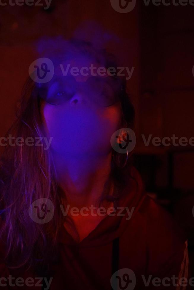 ritratto ravvicinato di una ragazza che svapa con una luce blu al neon foto