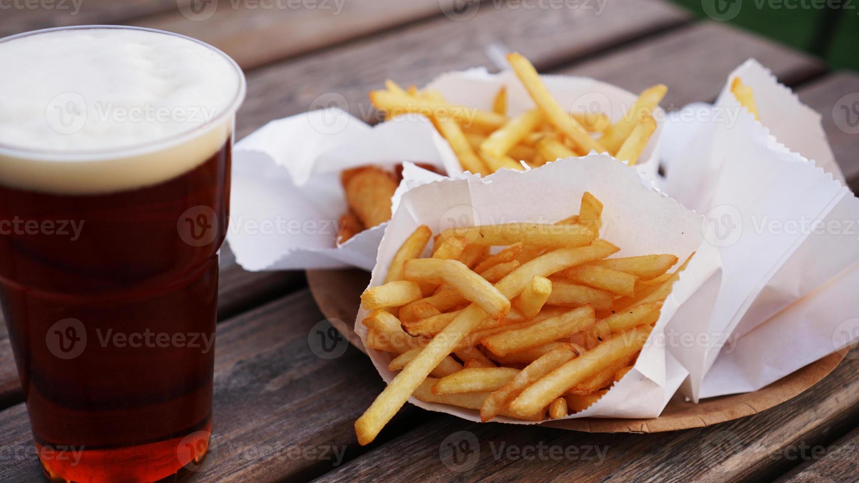 birra scura e patatine fritte su un tavolo di legno. punto ristoro. cibo da asporto foto