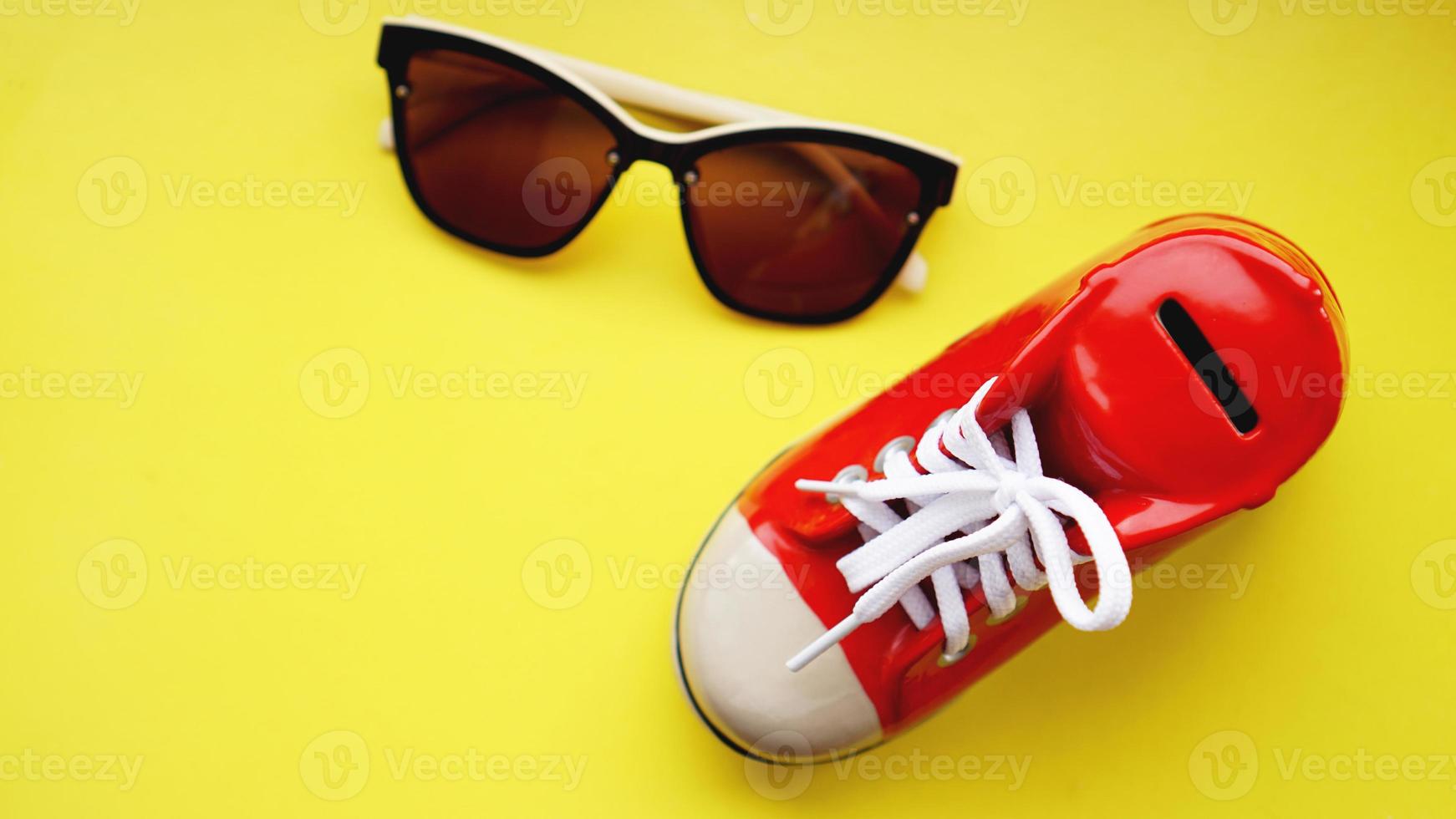 salvadanaio a forma di scarpe da ginnastica. occhiali da sole su sfondo giallo foto