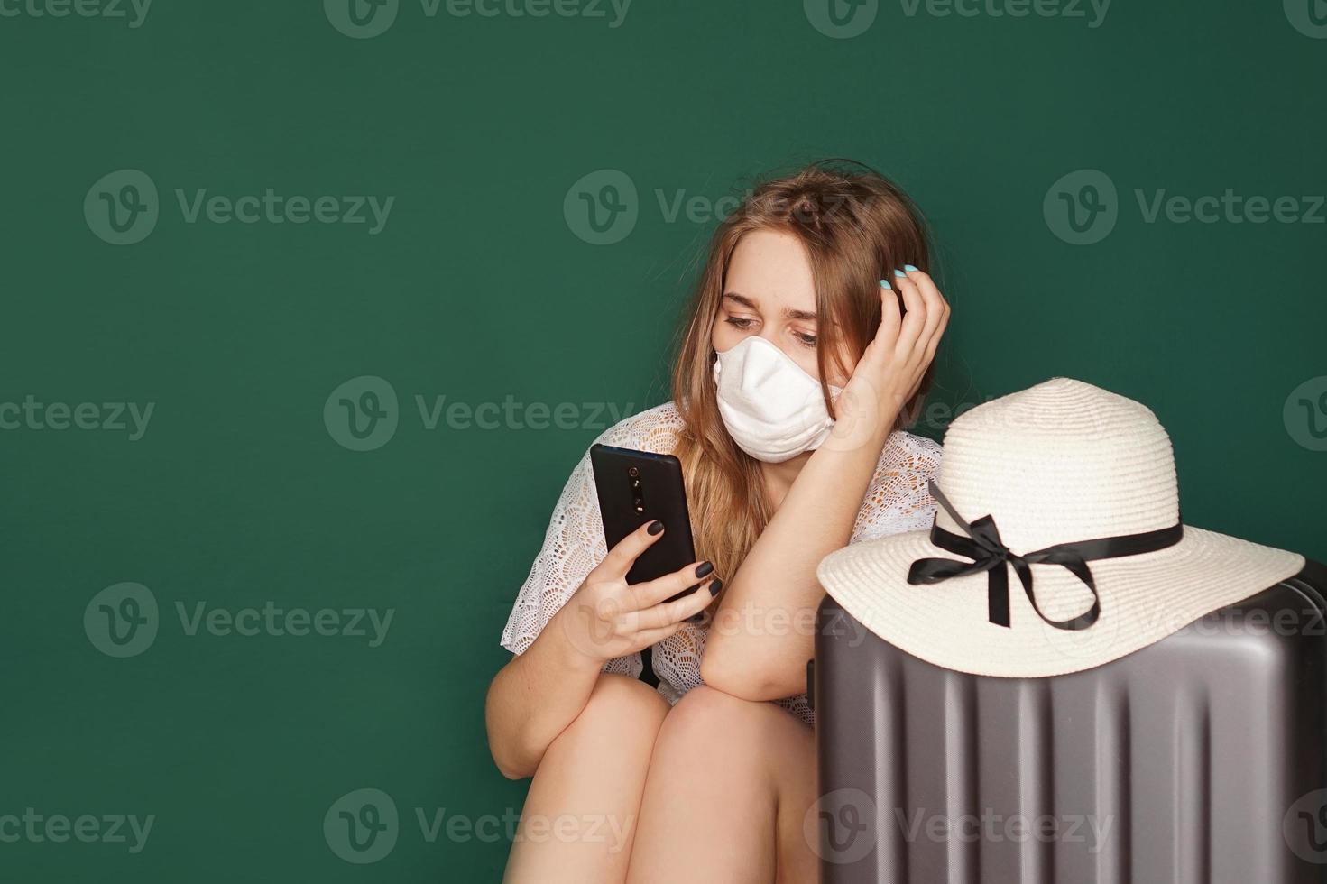 turista ragazza in una maschera medica si siede con i bagagli foto