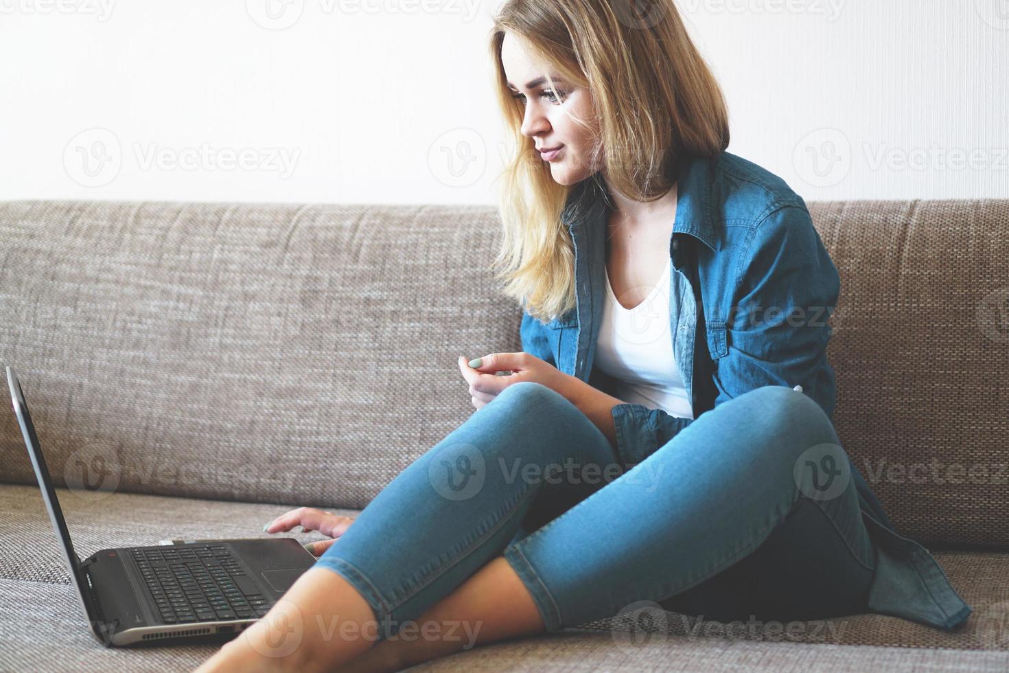 bionda sorridente che si rilassa sul divano con il suo laptop foto