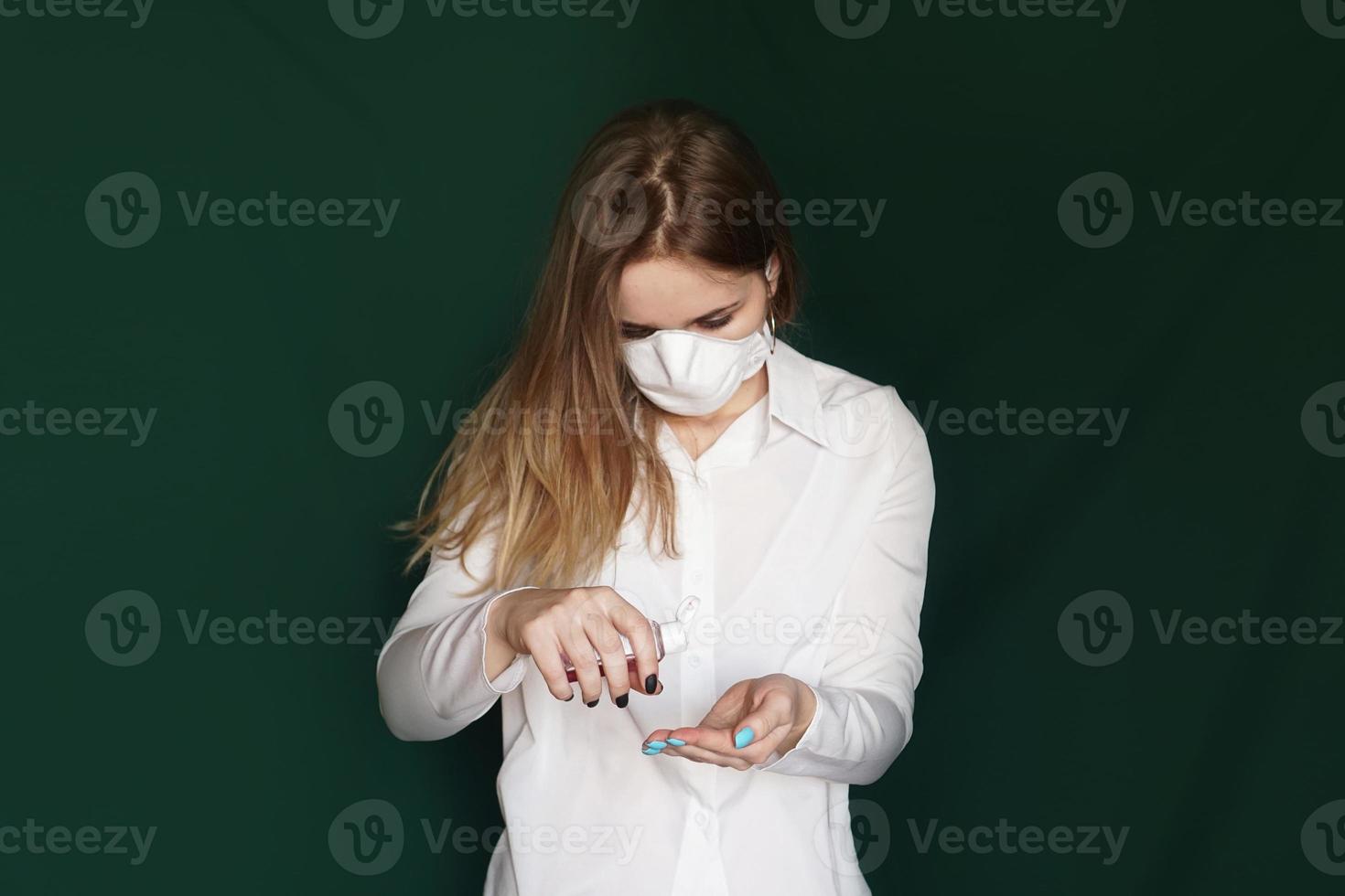 giovane ragazza bionda in una camicetta bianca e una maschera usa un antisettico foto