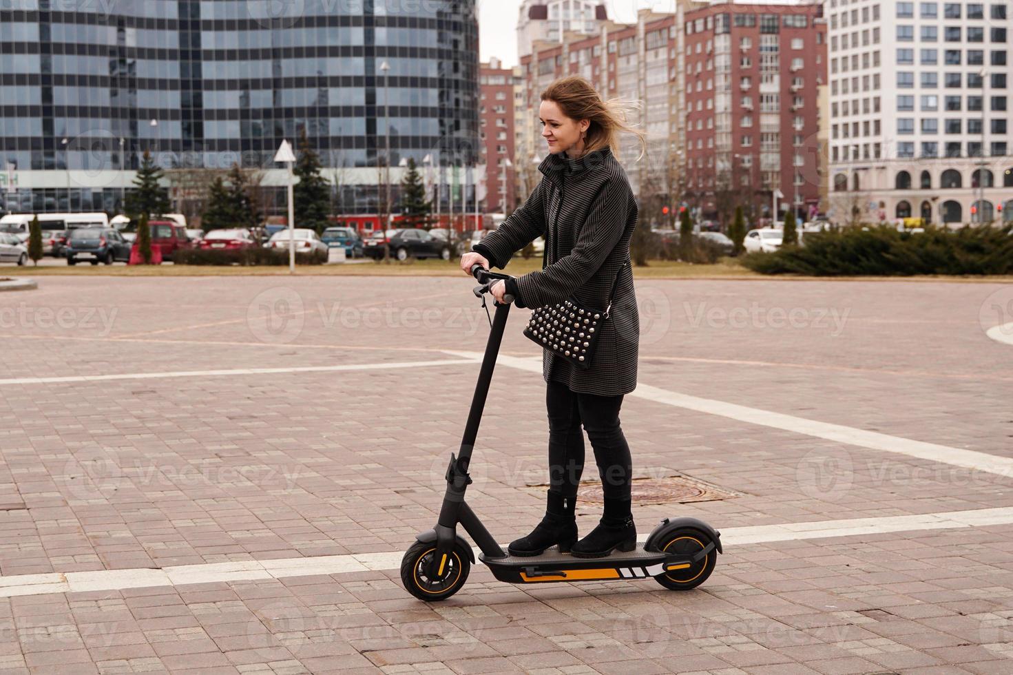 una bella ragazza con un cappotto guida uno scooter elettrico in giro per la città foto