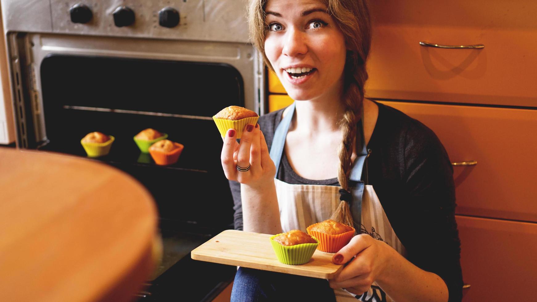 bella donna bionda che mostra muffin in cucina foto