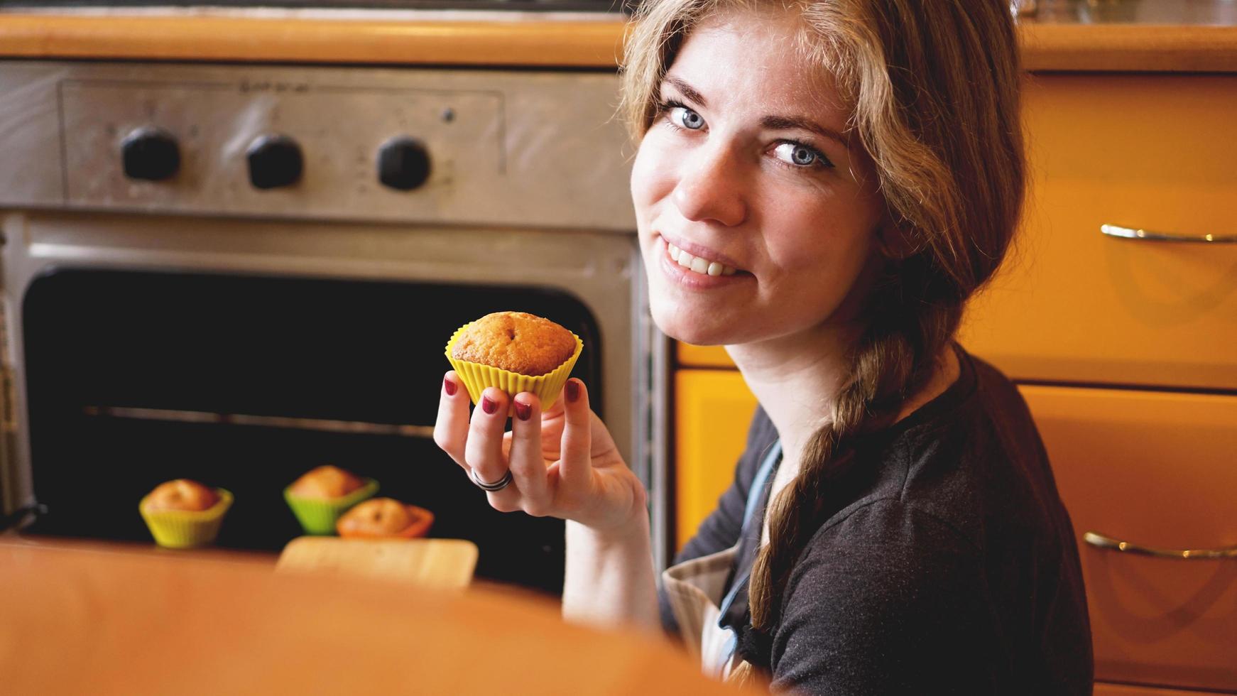 bella donna bionda che mostra muffin in cucina foto