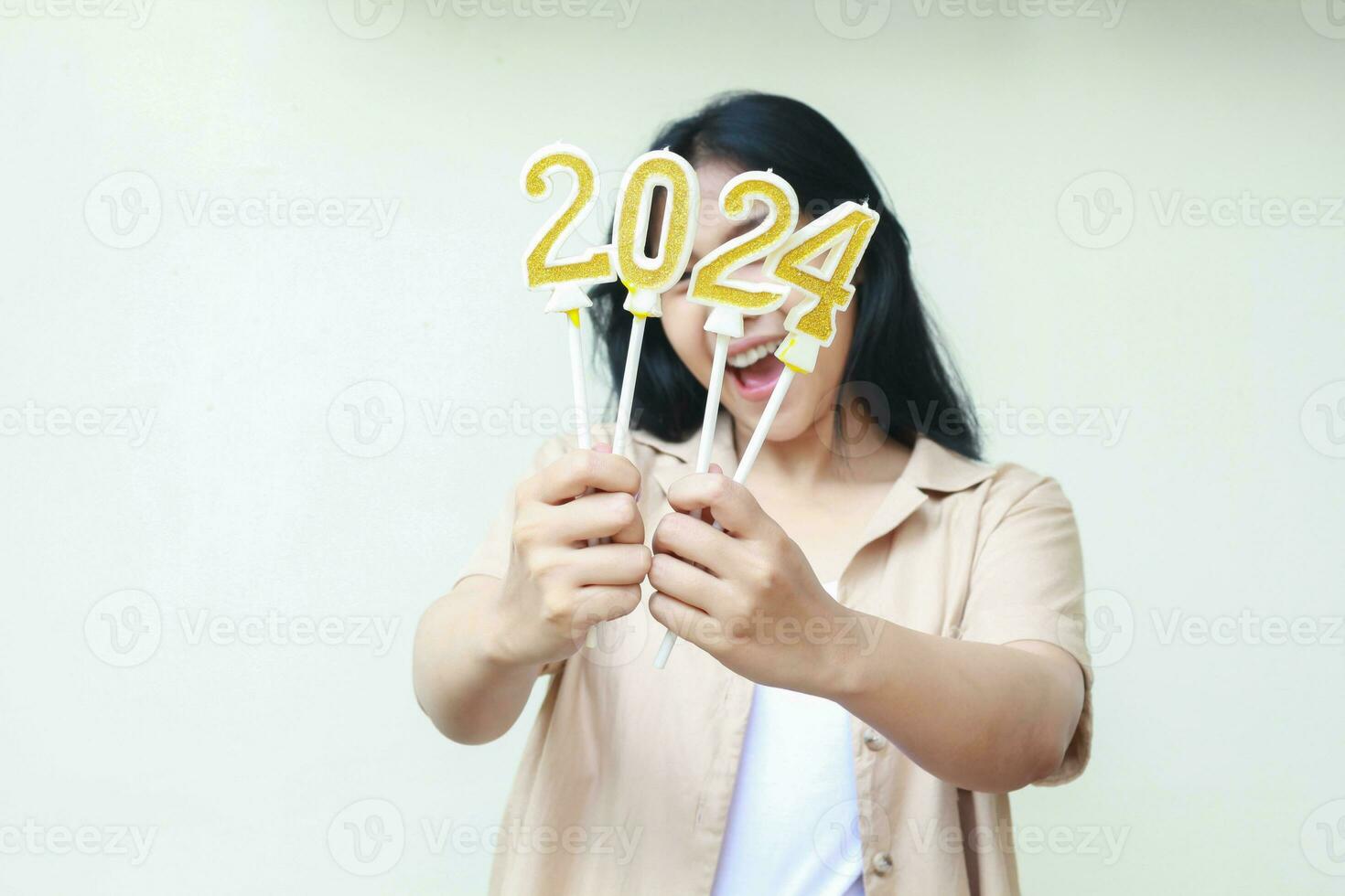 eccitato giovane donna asiatico mostrando d'oro candele numeri 2024 su mano per festeggiare nuovo anni vigilia indossare casuale Marrone Abiti isolato di bianca sfondo con copia spazio foto