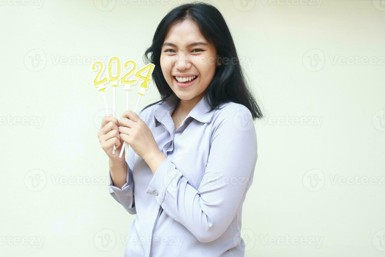 riuscito asiatico giovane donna imprenditore ridendo e sorridente per telecamera festeggiare 2024 nuovo anni di Tenere figura oro candele indossare grigio formale completo da uomo idolatrato di bianca sfondo foto