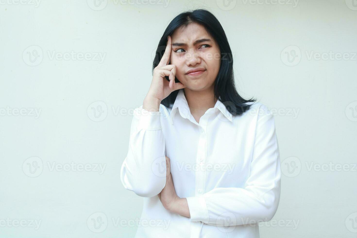 Immagine di meditando asiatico giovane donna bellissimo segretario guardare a parte stressato pensiero ufficio problema toccante sua testa e piegato braccia indossare bianca formale completo da uomo, in piedi foto