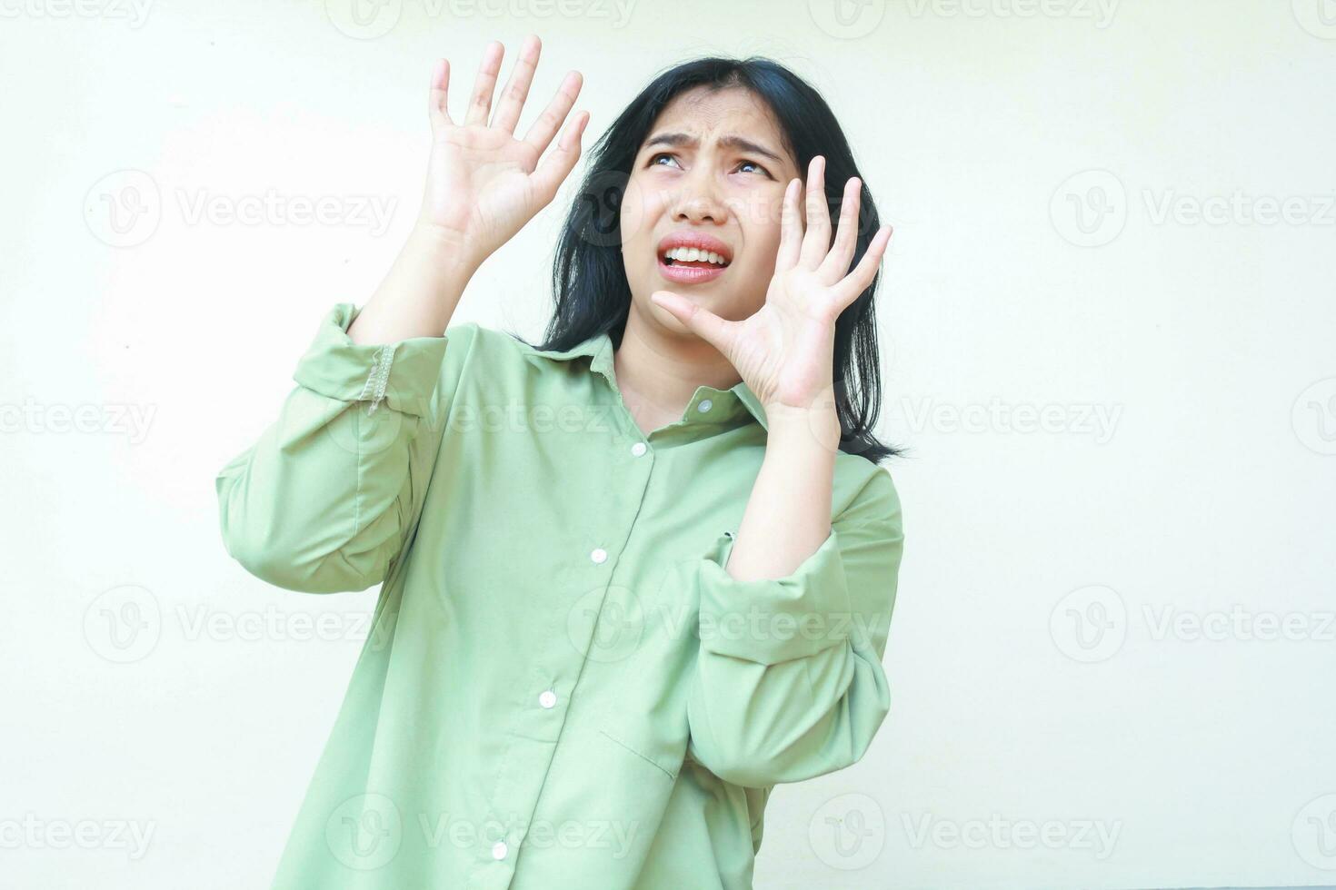 scioccato asiatico donna con buio capelli guardare sopra e raccolta palme per Prodotto caduto indossare verde sovradimensionato camicia isolato su bianca sfondo foto