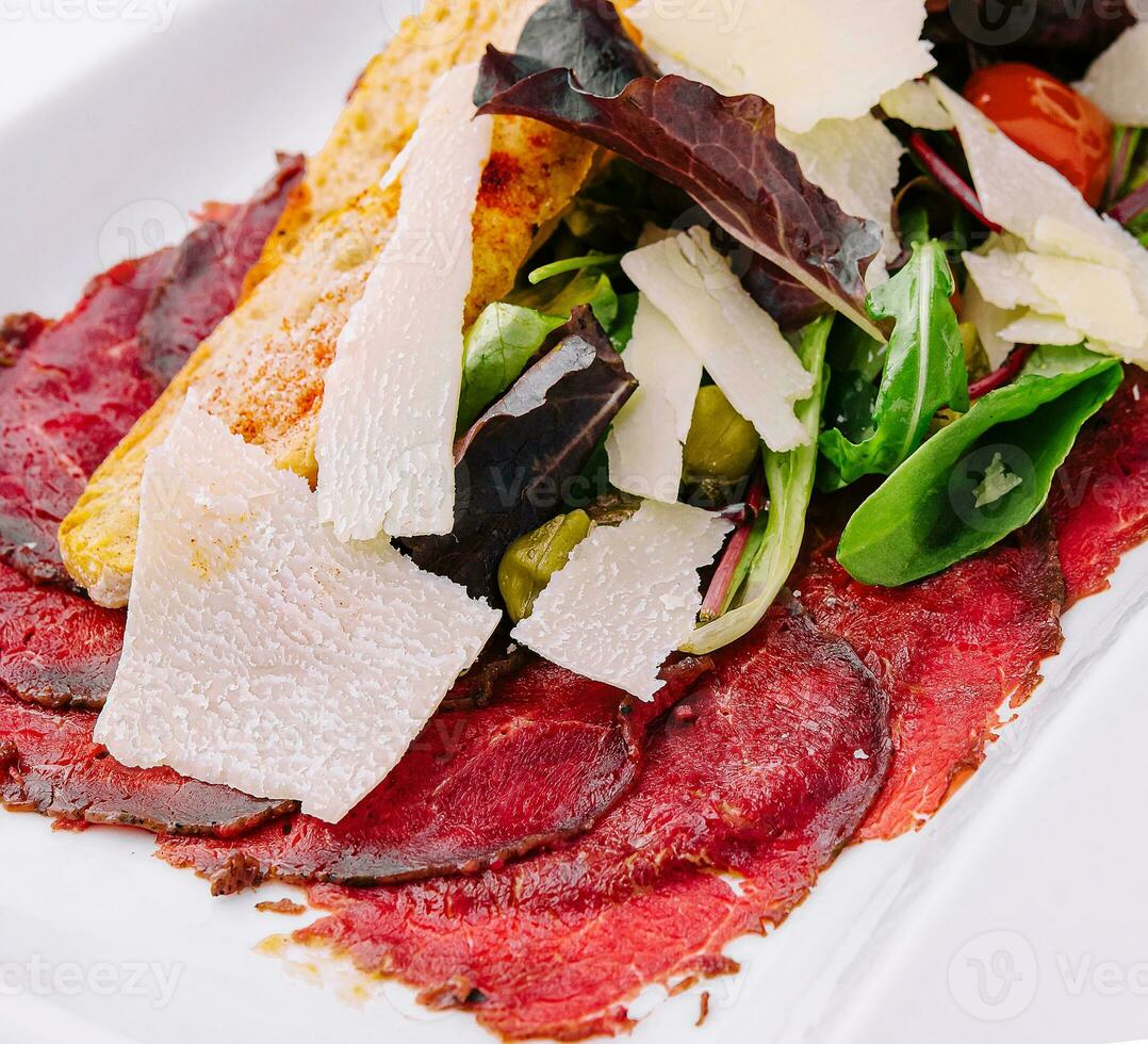 Manzo carpaccio con insalata e parmigiano su un' bianca piatto foto