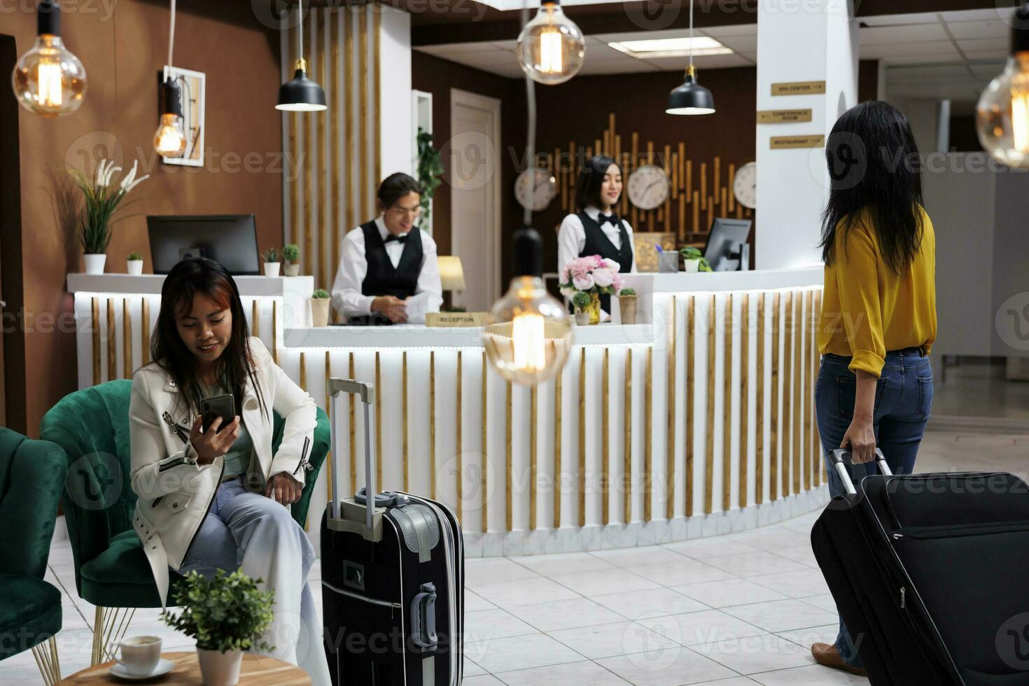 ospiti arrivo su vacanza e siamo in piedi a accogliente Hotel Ingresso con bagagli, preparazione per essere verificato in. confortevole Hotel atrio con nuovo i clienti e Due asiatico receptionist foto