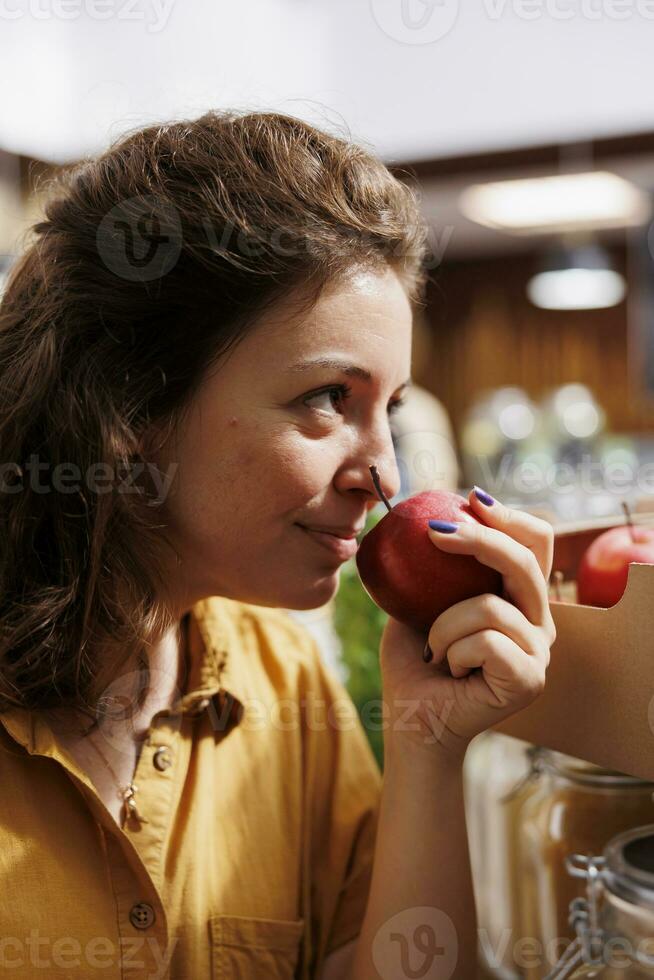 fricchettone donna odorare bio azienda agricola cresciuto mele nel zero rifiuto memorizzare con Basso carbonio orma. sorridente cliente analisi per vedere Se Locale Quartiere negozio frutta siamo fresco e sostanze chimiche gratuito, vicino su foto