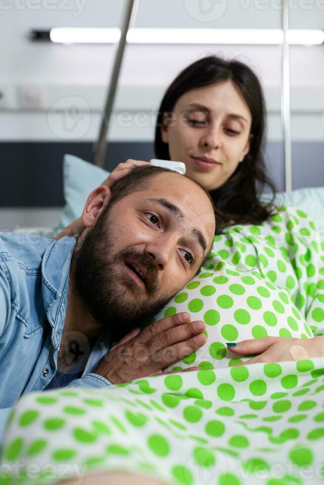 allegro futuro padre in piedi con testa su donna gonfiarsi, parlando con bambino prima cesareo chirurgia nel ospedale reparto. incinta paziente preparazione per consegna bambino nel maternità servizio, struttura foto